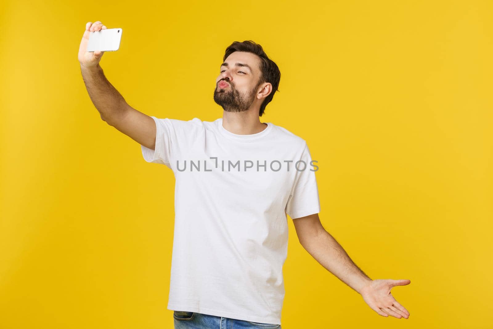 Closeup of young handsome man looking at smartphone and taking selfie. isolate over yellow background