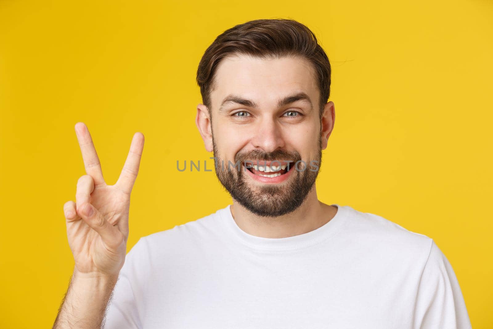 Young handsome man wearing striped t-shirt over isolated yellow background smiling looking to the camera showing fingers doing victory sign. Number two by Benzoix