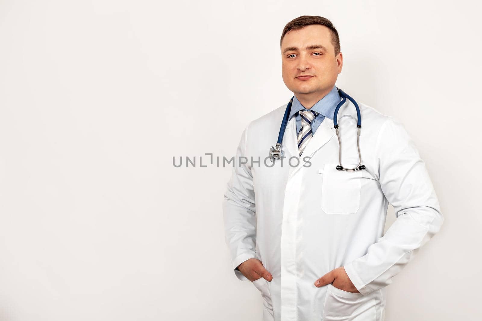 Portrait of smiling young male doctor with a stethoscope around neck standing within a white coat, isolated on gray background