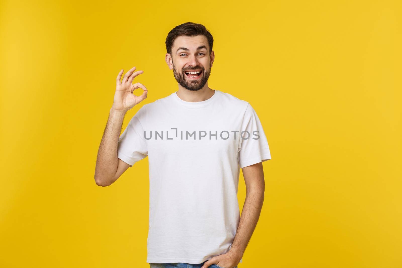 Portrait of a cheerful young man showing okay gesture isolated on yellow background by Benzoix