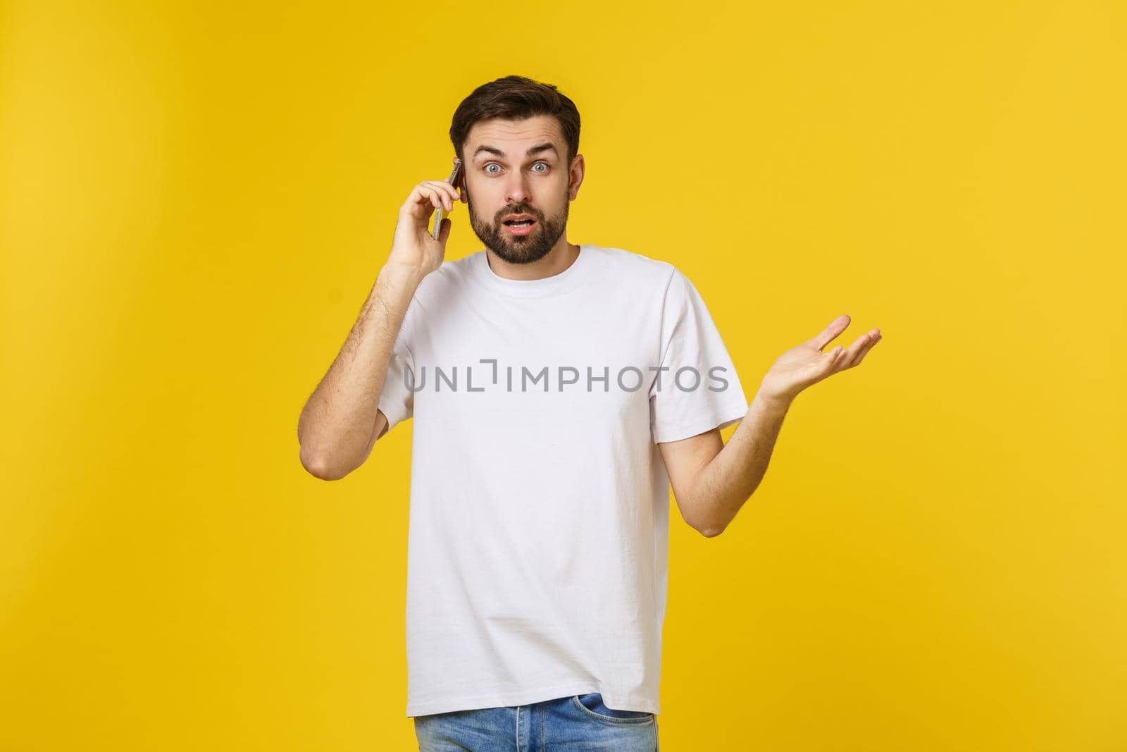 Portrait of a serious man talking on the phone isolated on a yellow background. Looking at camera by Benzoix