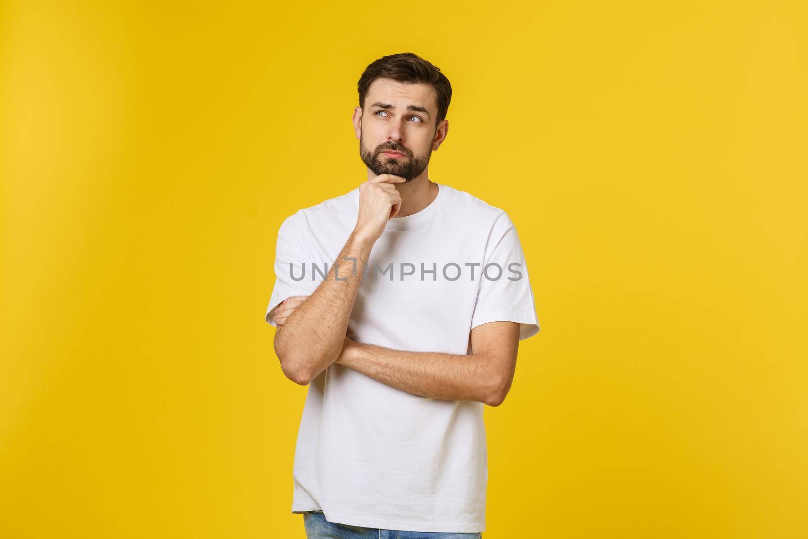 Pensive curious man looking up in thinking pose trying to make choice or decision isolated on yellow background