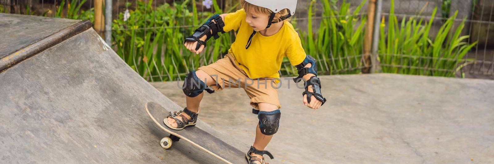 Athletic boy in helmet and knee pads learns to skateboard with in a skate park. Children education sports. BANNER, LONG FORMAT
