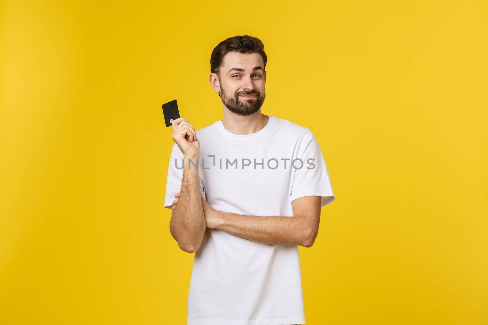 Happy smiling young man showing credit card isolated on yellow background.