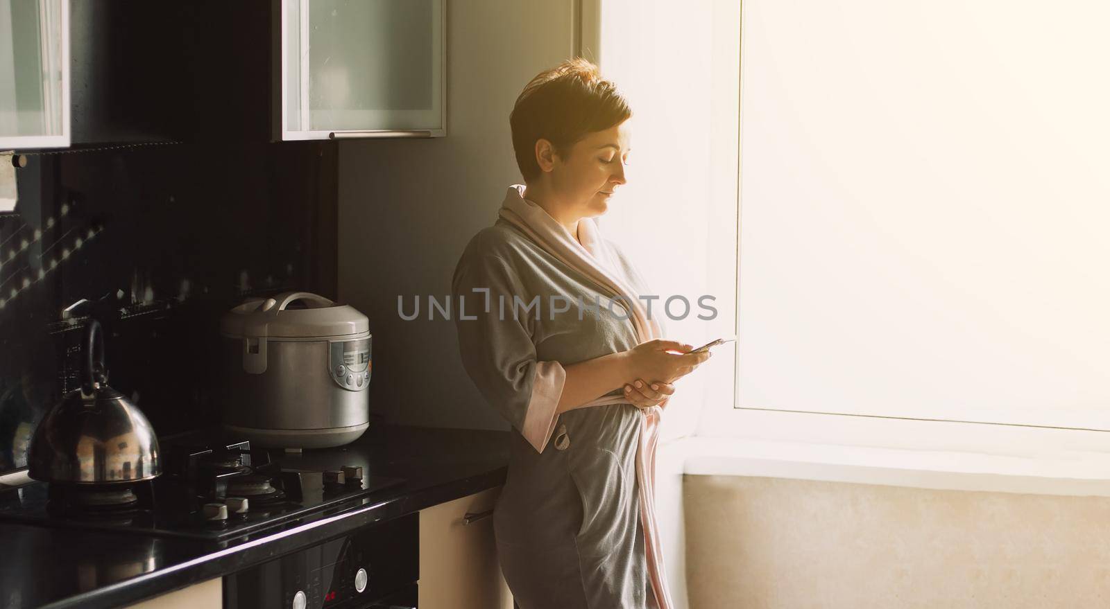 Work from home. Pretty woman in a bathrobe in the kitchen in the morning communications and works on the phone at home. Working at home