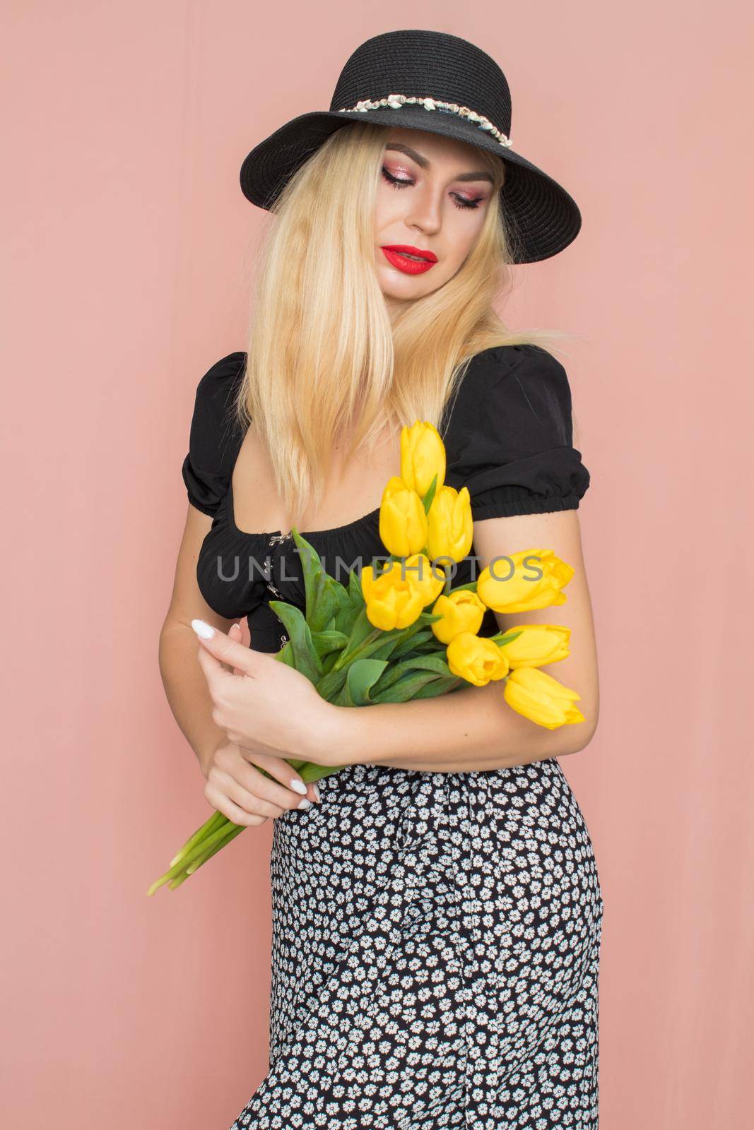 Blonde woman in black hat holding yellow tulips by Bonda