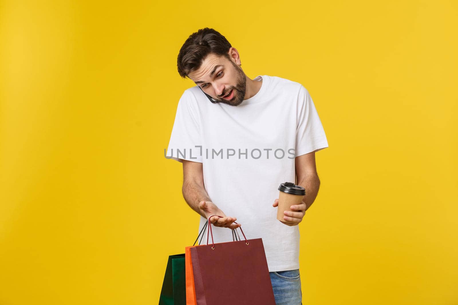 Mobile app for online shopping. Joyful happy man in casual white t-shirt holding cell phone and packages, smiling at camera. by Benzoix
