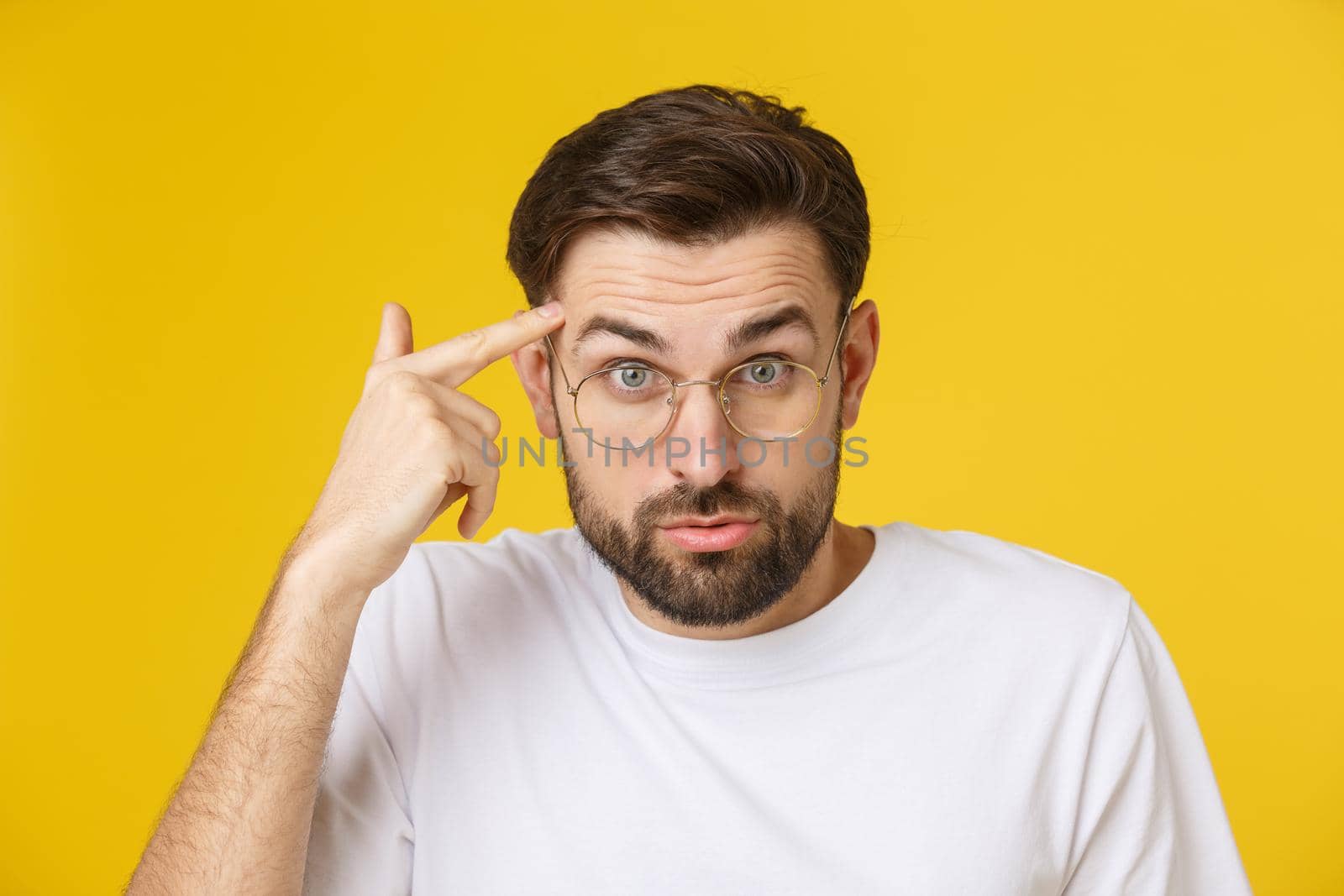 Closeup of young handsome man looking and showing funny face at camera, wearing glass. Isolated view on yellow background