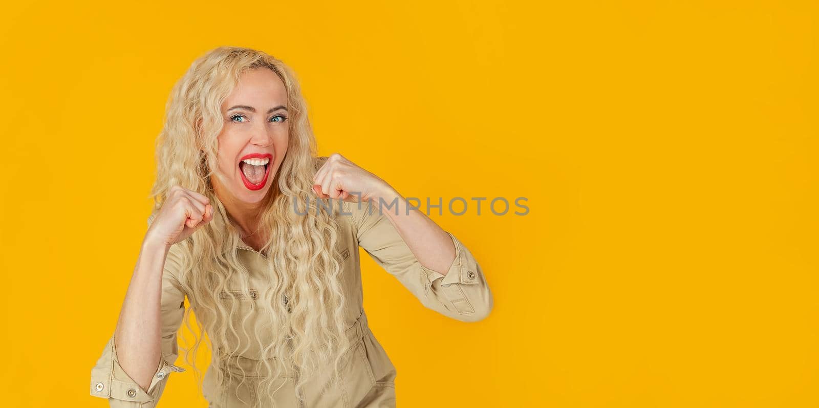 Cheerful, happy woman, raising her hands with her fist, cheering for the team, winning a huge bet, playing in the casino in delight, cheering friends, watching football, yellow background