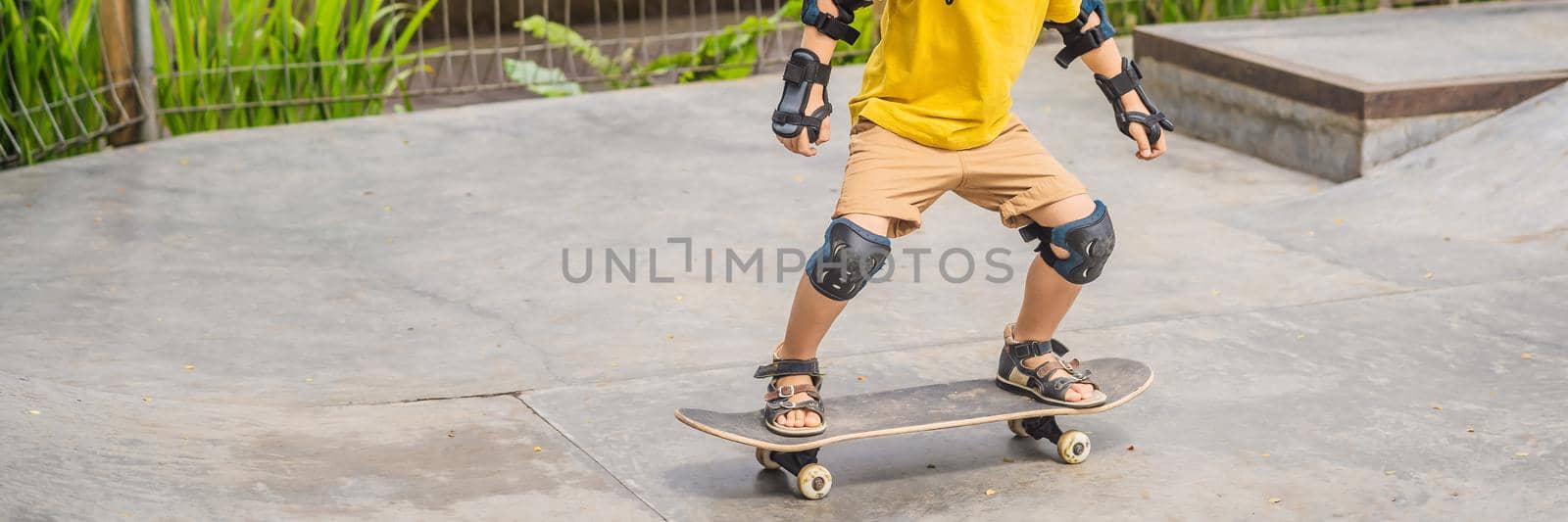 Athletic boy in helmet and knee pads learns to skateboard with in a skate park. Children education sports. BANNER, LONG FORMAT