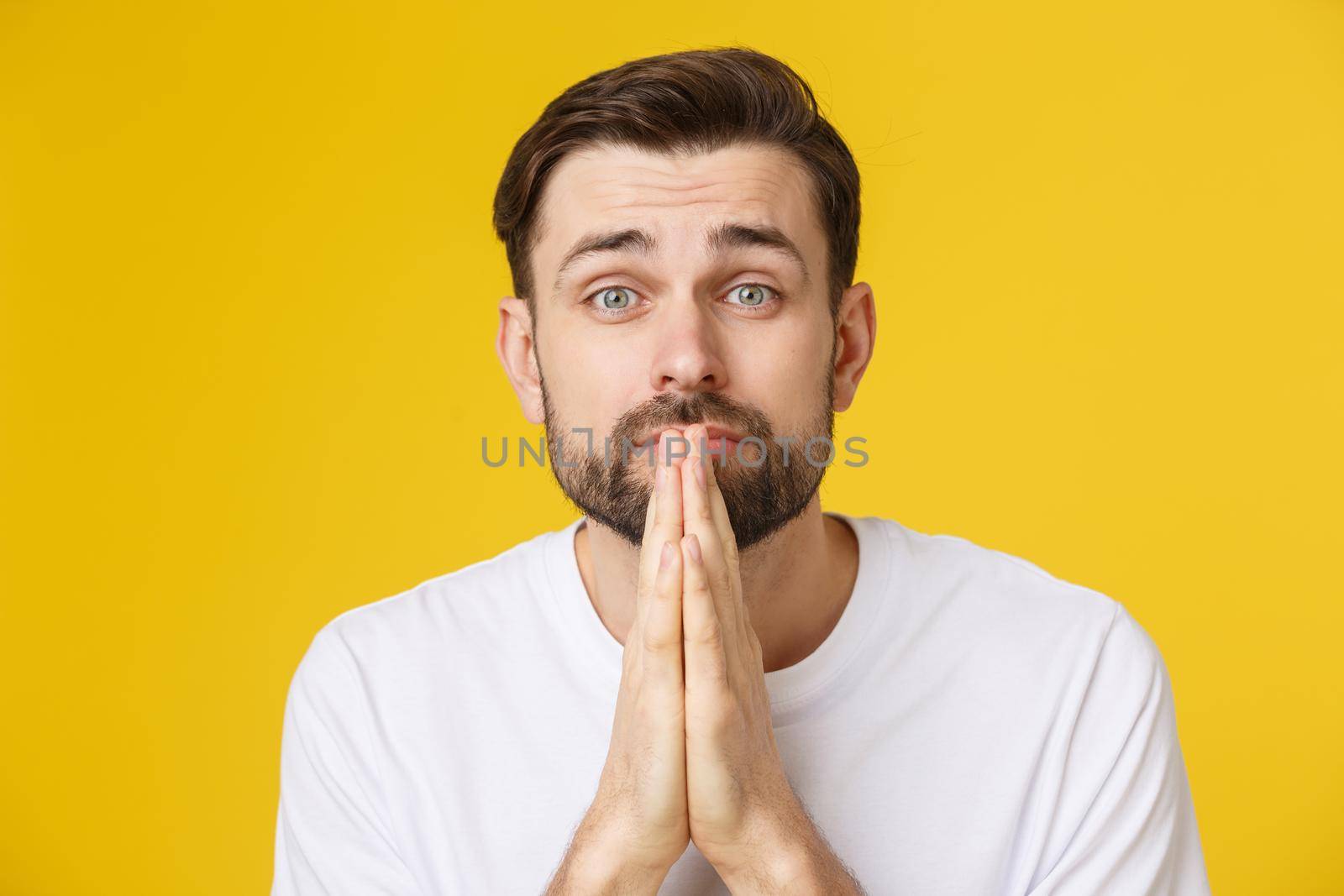 Young guy dressed casually isolated on yellow background, having put hands together in prayer or meditation, looking relaxed and calm