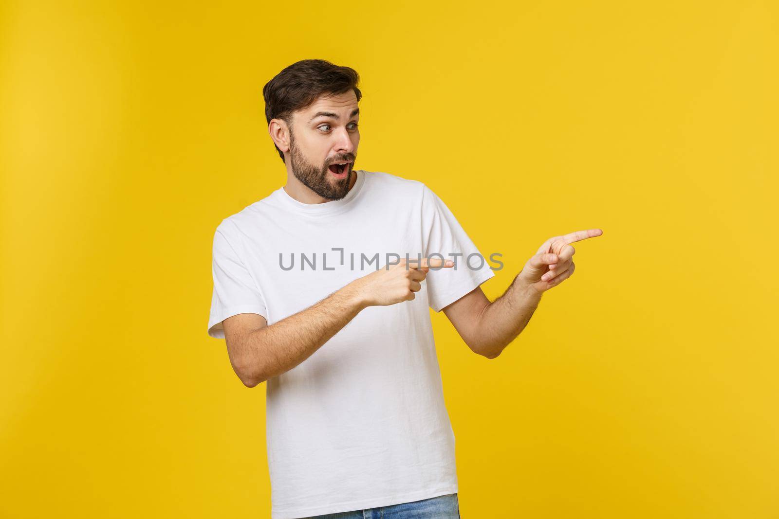 Man pointing showing copy space isolated on yellow background. Casual handsome Caucasian young man. by Benzoix