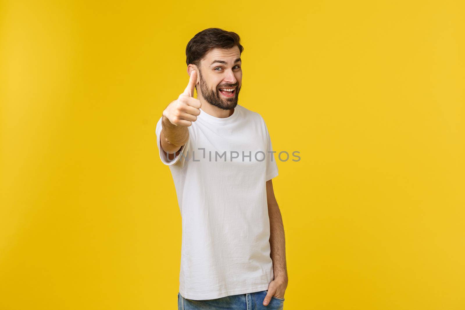 Young happy man with thumbs up sign in casuals isolated on yellow background.