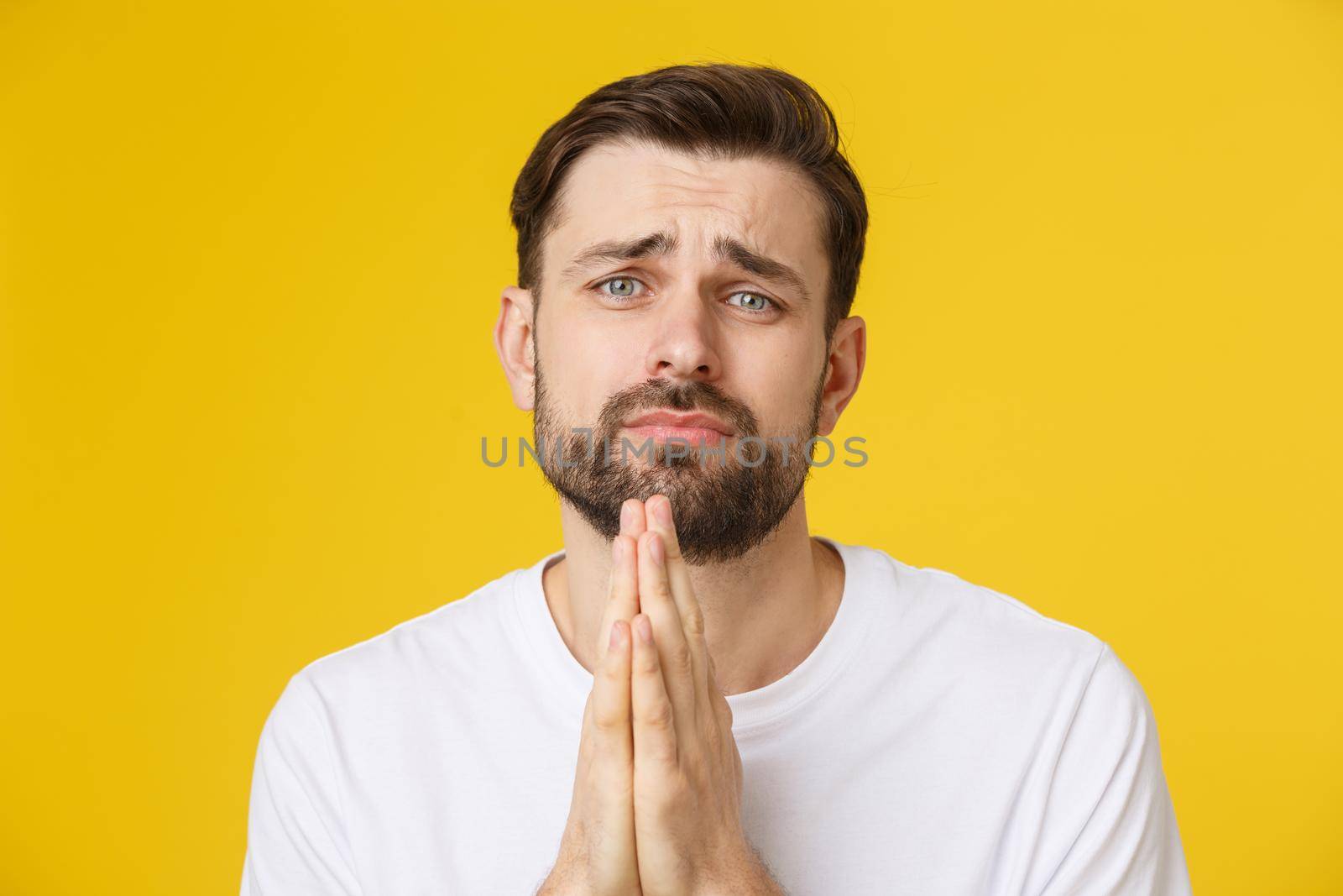 Young guy dressed casually isolated on yellow background, having put hands together in prayer or meditation, looking relaxed and calm
