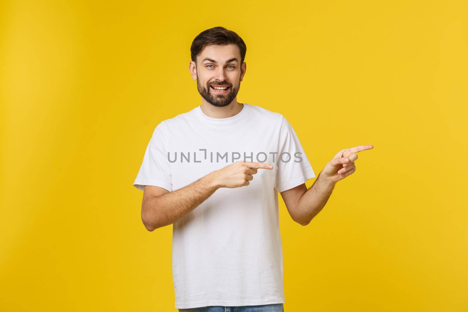 Man pointing showing copy space isolated on yellow background. Casual handsome Caucasian young man