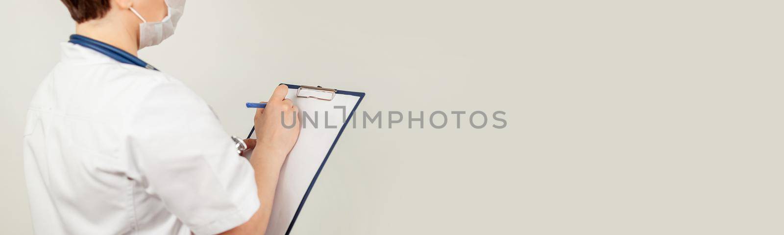 Female doctor writes with a pen a document on a tablet, writes a medical history. The concept of healthcare, medicine and pharmacy.