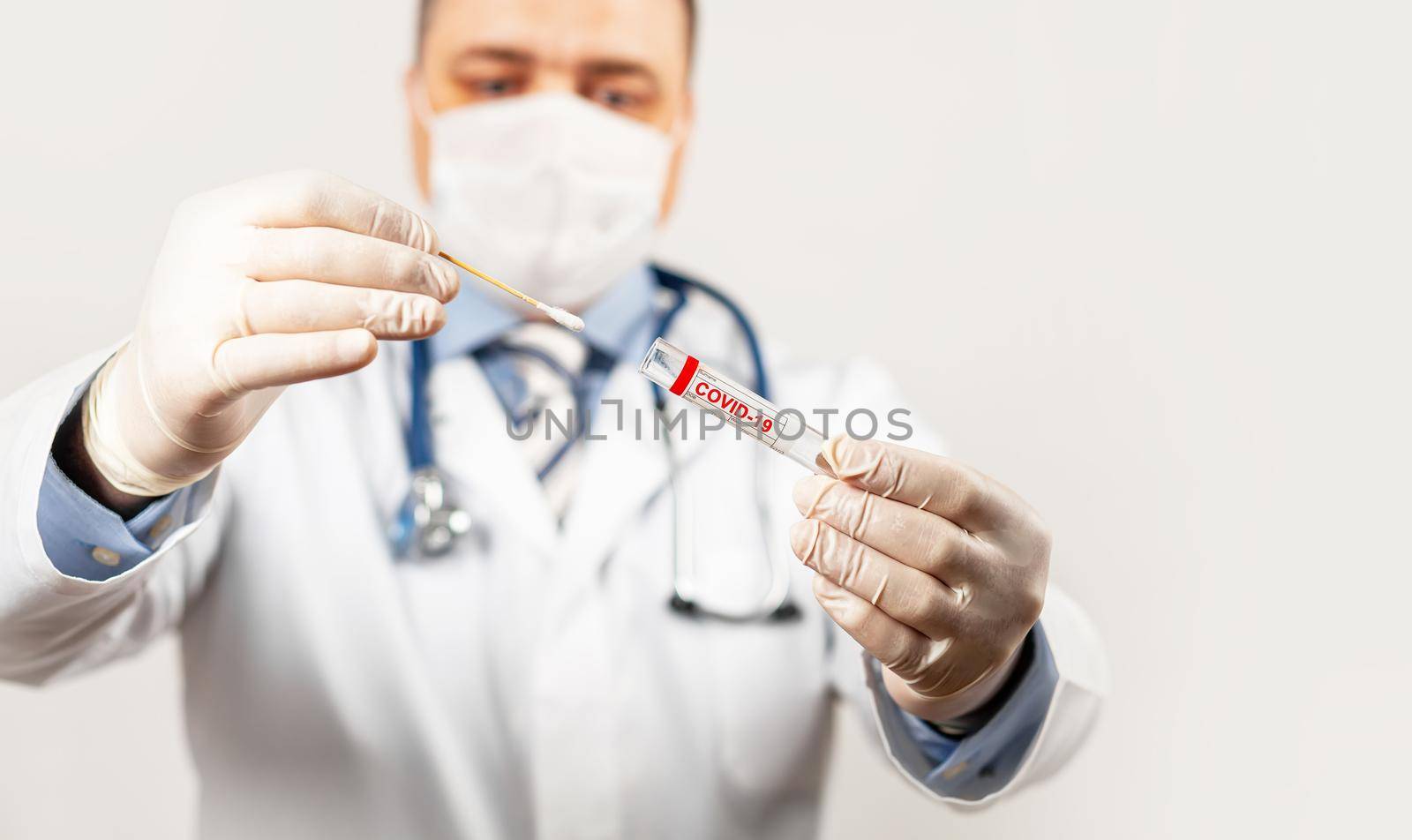 Test for coronavirus Covid-19. Male doctor or nurse doing nasal swab laboratory analysis in a hospital laboratory. A medical technologist holds a COVID-19 smear kit by wearing protective gloves.
