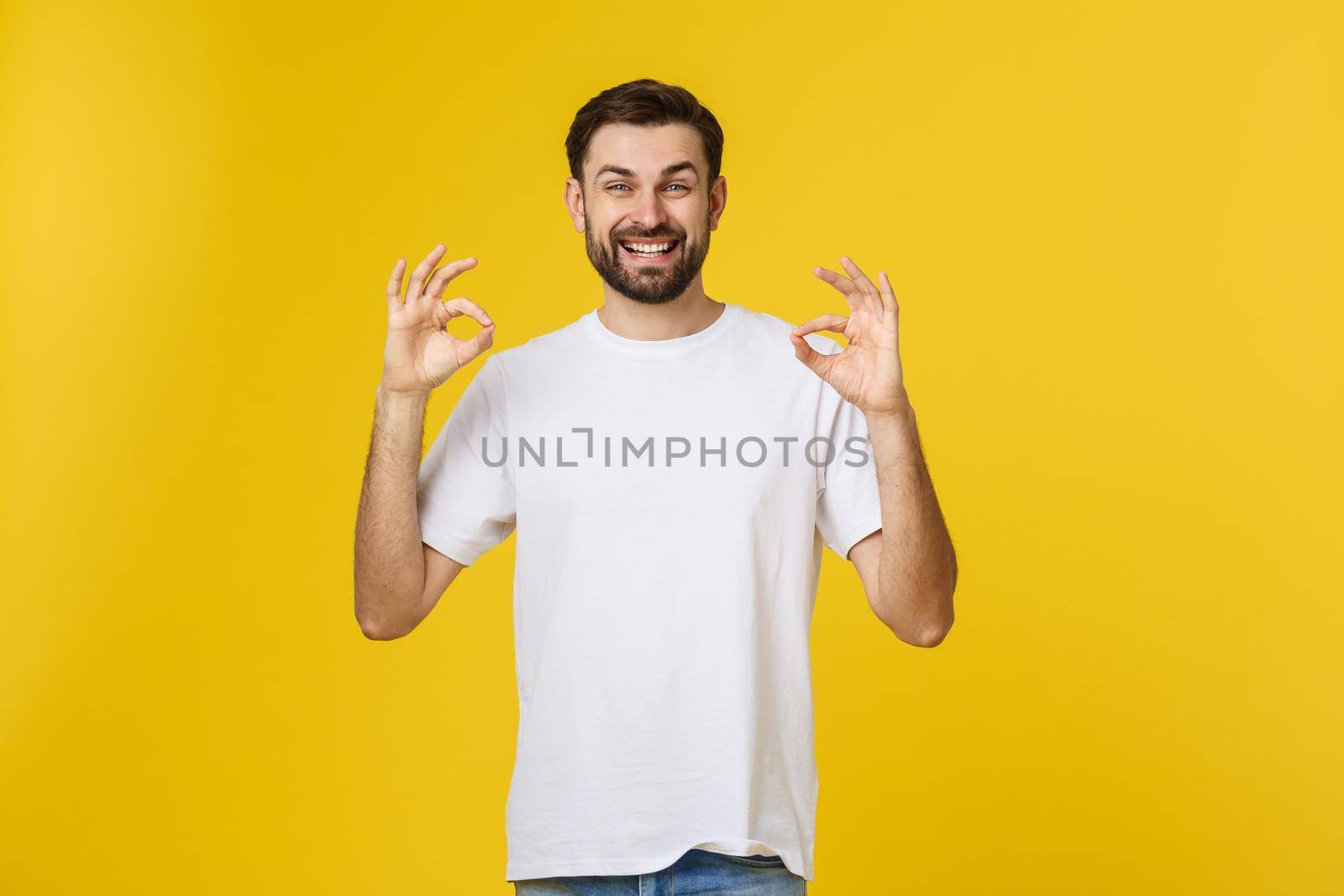 Portrait of a cheerful young man showing okay gesture isolated on yellow background by Benzoix