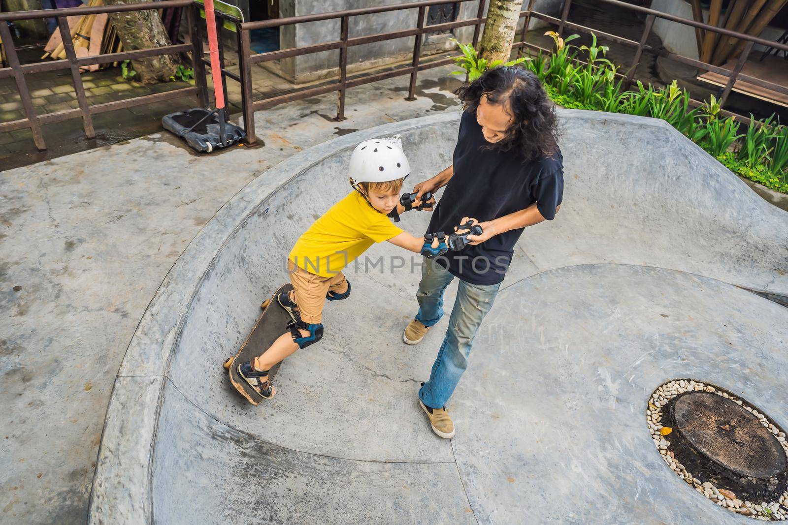 Athletic boy learns to skateboard with asian trainer in a skate park. Children education, sports. Race diversity.