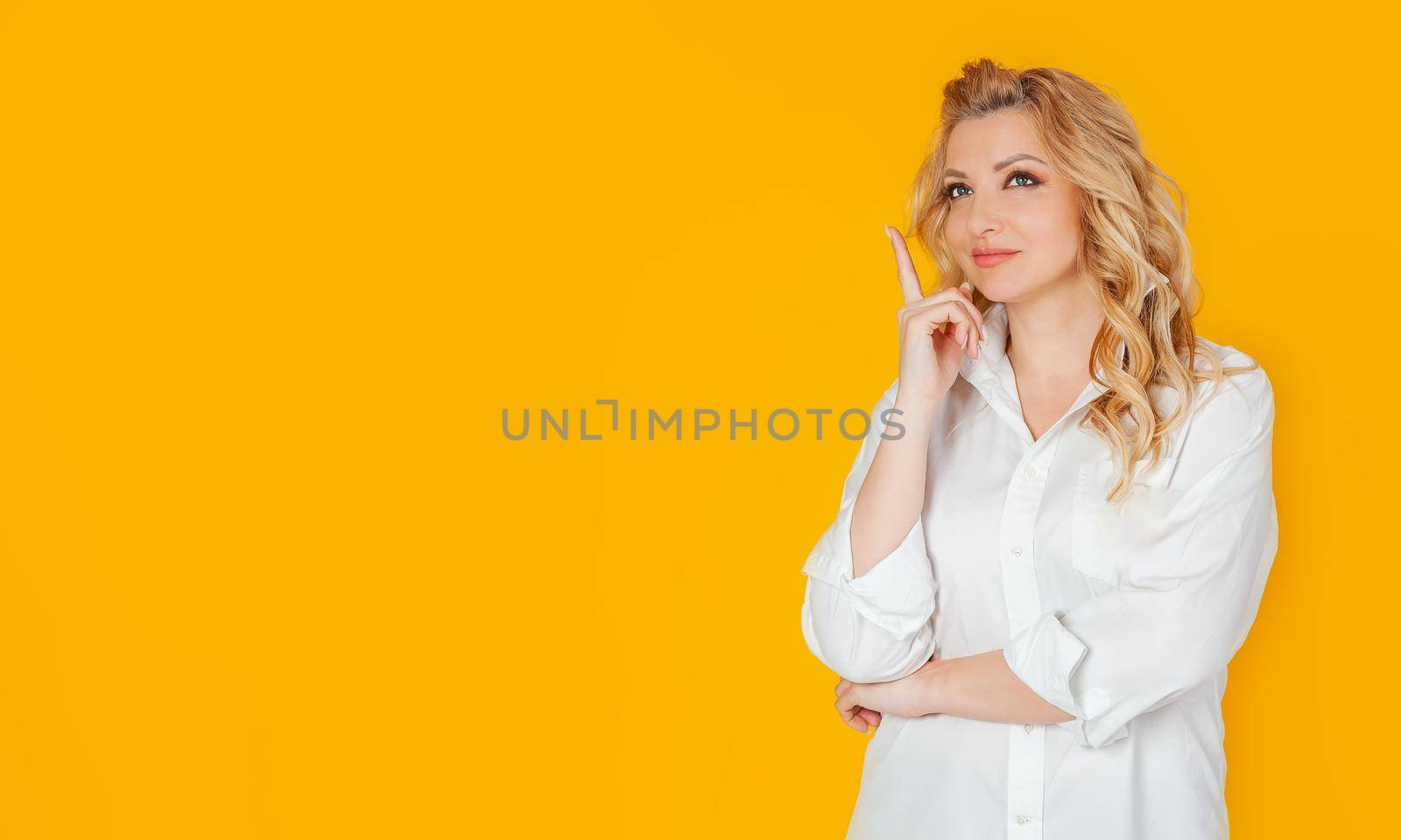 Young pretty girl holding a finger up having a good idea, pointing with a finger, happy smiling woman having an idea on yellow background. Copy space template