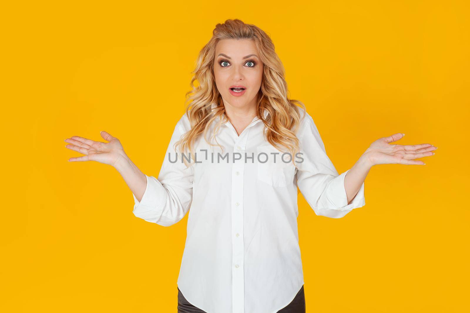 A clumsy European blonde woman in a white shirt, shrugging her shoulders to the sides, not suspecting, asks, perplexed, uncertain expression on her face, ignorant to say, Oh, sorry, I didn't know.