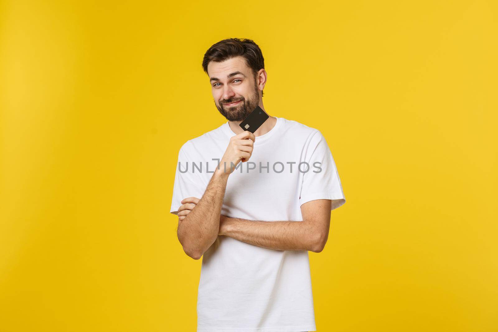 Happy smiling young man showing credit card isolated on yellow background by Benzoix