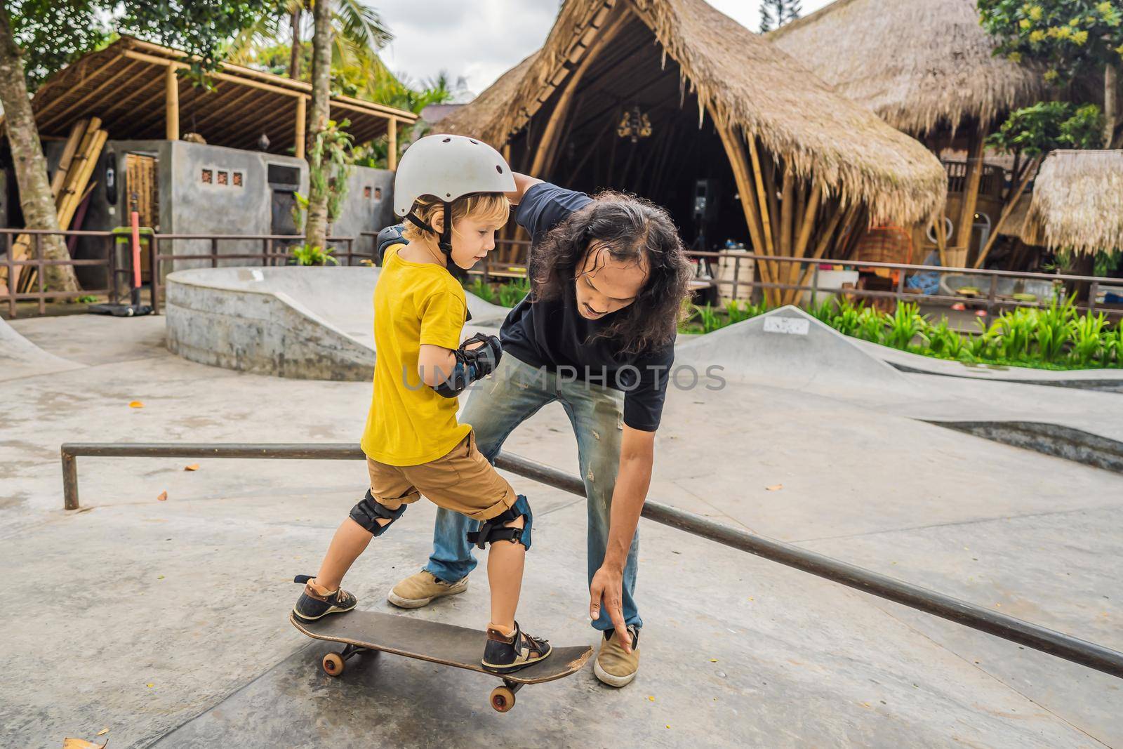 Athletic boy learns to skateboard with asian trainer in a skate park. Children education, sports. Race diversity.