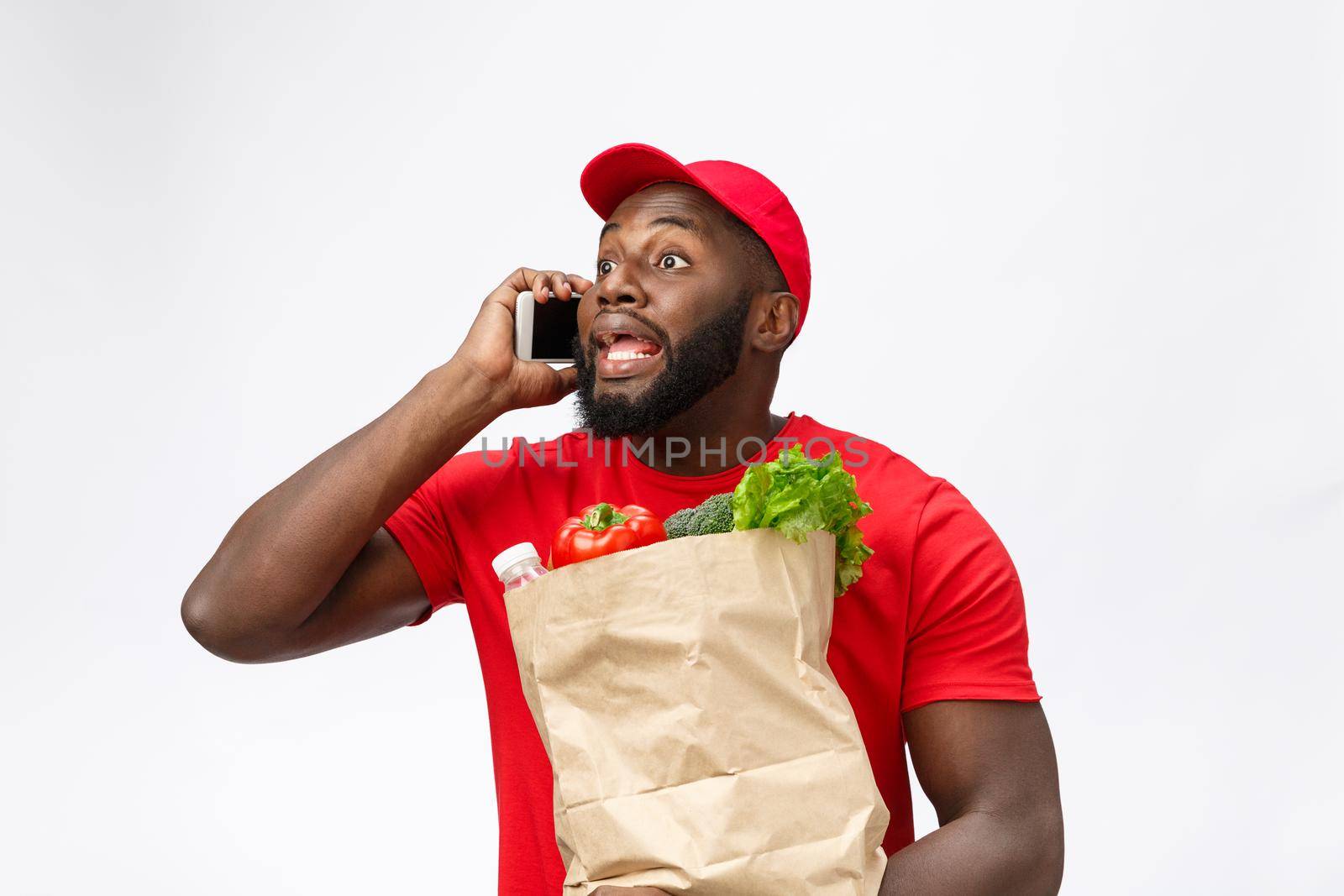 Delivery Concept - Portrait of Handsome African American delivery man or courier with grocery package and talking on mobile phone to check the order. Isolated on Grey studio Background.