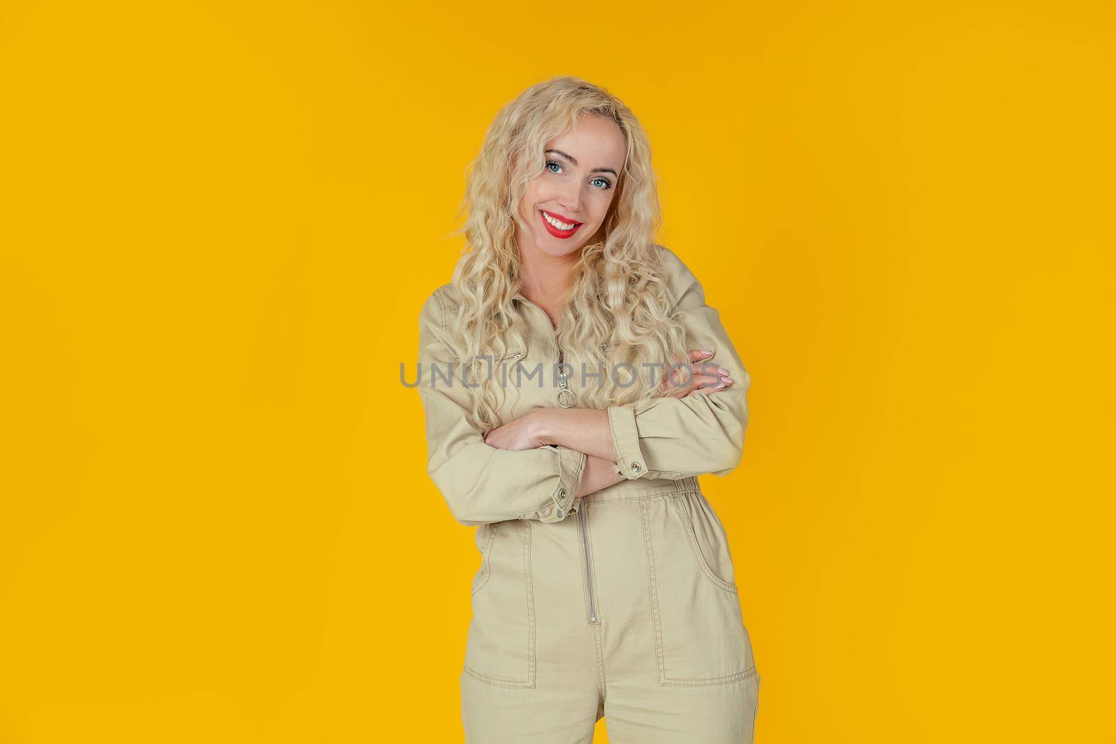Portrait of a joyful and cheerful cute European curly-haired blonde woman who jokes cheerfully, entertains the conversation, smiles and laughs at the camera over the yellow wall. What a wonderful day