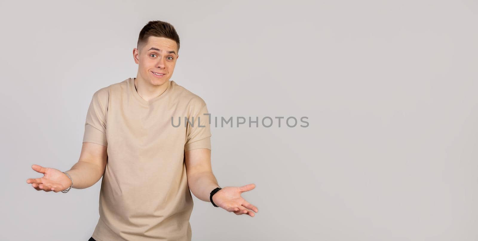 A handsome young guy a man smiles and shrugs spreading hands, does not know what to say in response. Language of the body. Looks at the camera.