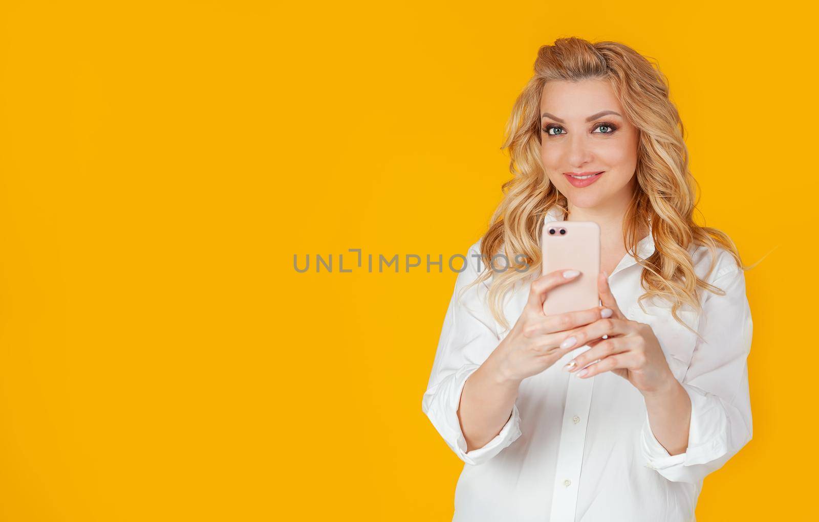 Excited carefree european girl blogger takes photos of girlfriend using smartphone, holds camera, looks at camera, smiles, moment on social networks, blogger captures moment
