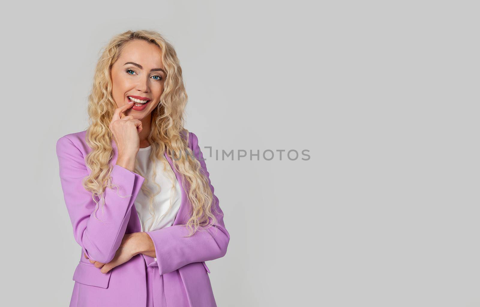 Attractive charismatic blonde woman with blue eyes laughing joyfully biting her finger, smiling contented, winning a university exchange program, smiling happily on a white background