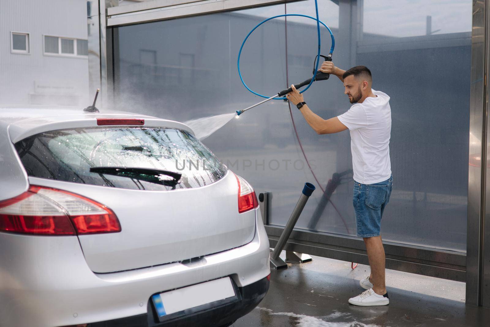 Back view of young man cleaning his car with a jet sprayer. Self service car washing.