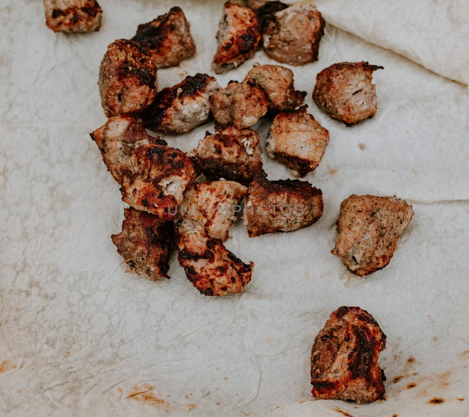 Pork veal cow meat cut into square pieces and fried over a fire lies on a thin white pita bread.