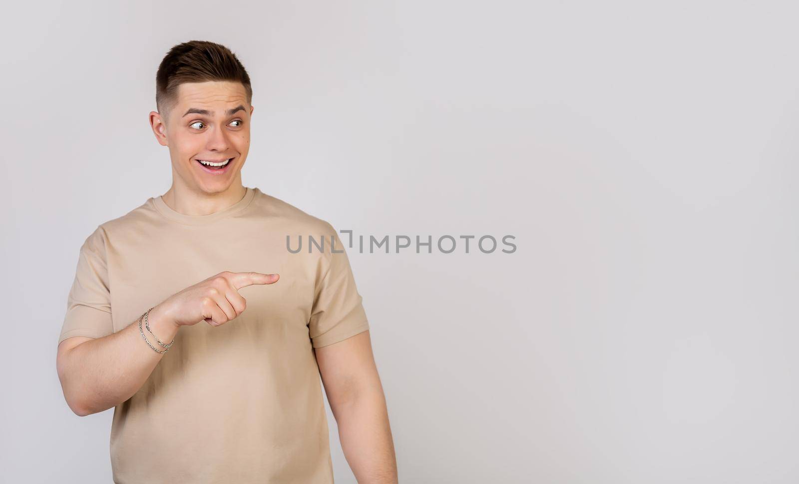 Handsome strong young man pointing finger to the right with a surprised expression on his face. Copy ad space