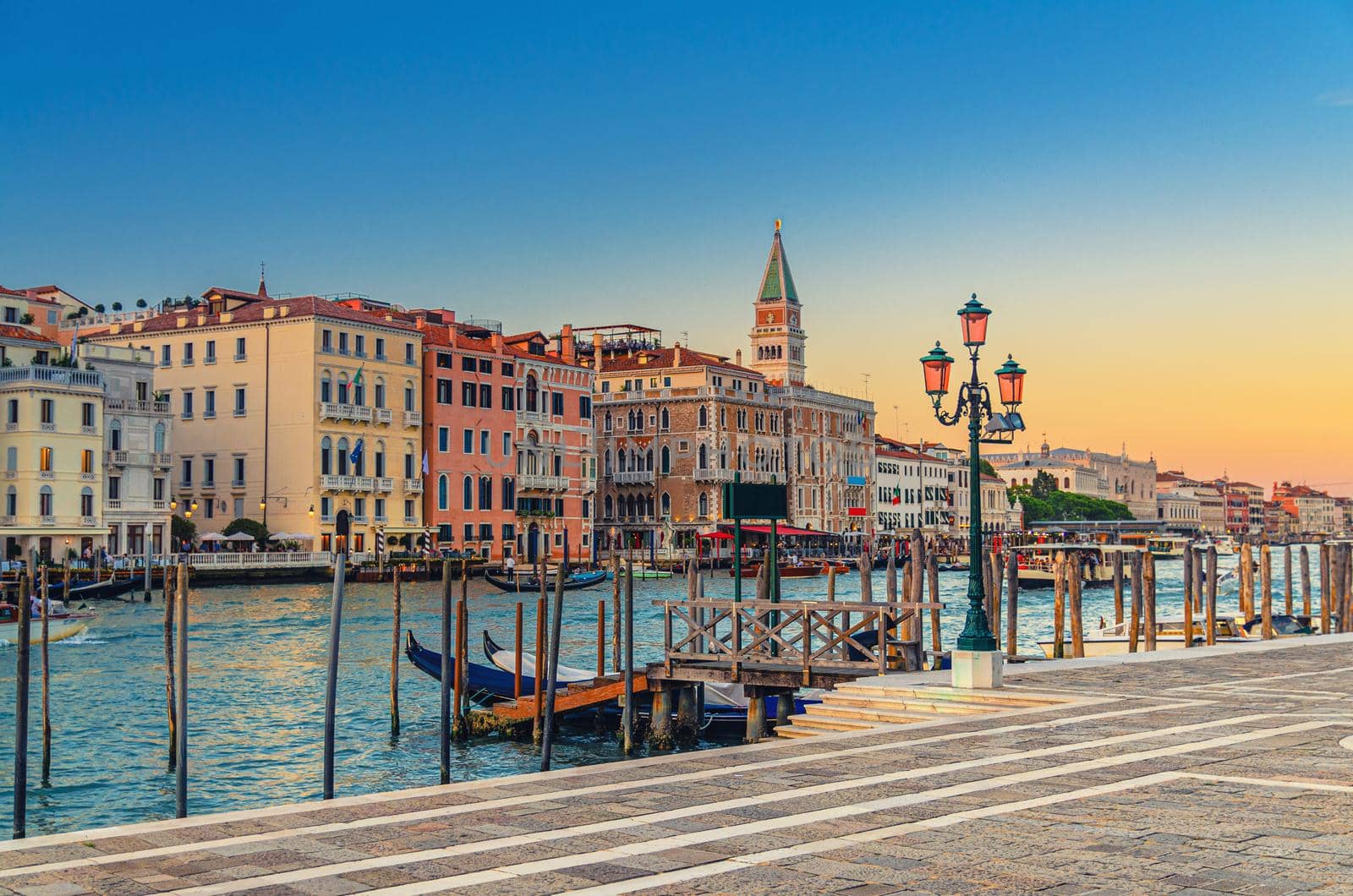 Venice evening view with Fondamenta Salute embankment promenade near pier of Grand Canal waterway at sunset, Campanile bell tower and row of baroque style buildings in San Marco sestiere, Italy