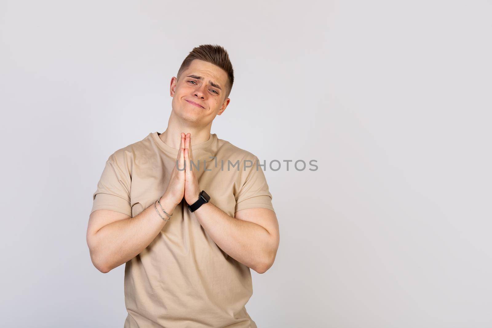 Handsome young man holding his palms pressed together, asking for forgiveness after a quarrel, looking at the camera. Language of the body