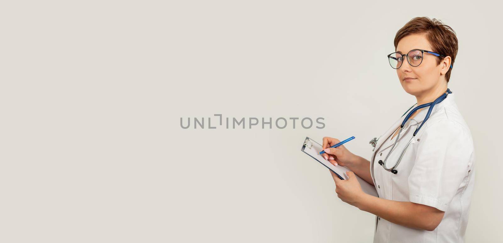 Female doctor writes with a pen a document on a tablet, writes a medical history. The concept of healthcare, medicine and pharmacy.