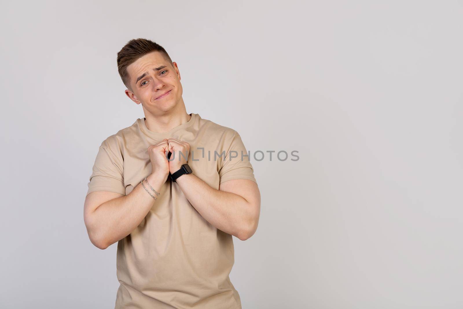 Handsome young man holding his palms pressed together, asking for forgiveness after a quarrel, looking at the camera. Language of the body