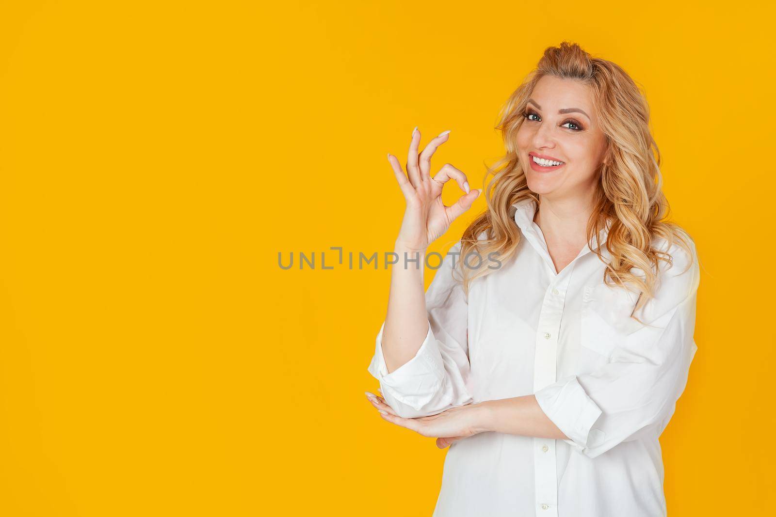 Charismatic self-confident cheerful, gorgeous adult woman, dressed in a white shirt, smiling broadly, showing a good gesture, excellent mood, guaranteeing everything amazing