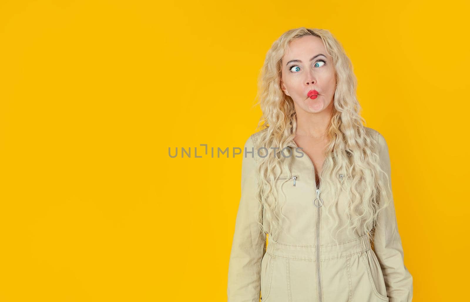 Amusing, playful cute woman, showing her cheerful side, playing charades, imitating fish, folding her lips and squinting, turning her eyes, standing on a yellow background, cheerfully grimacing