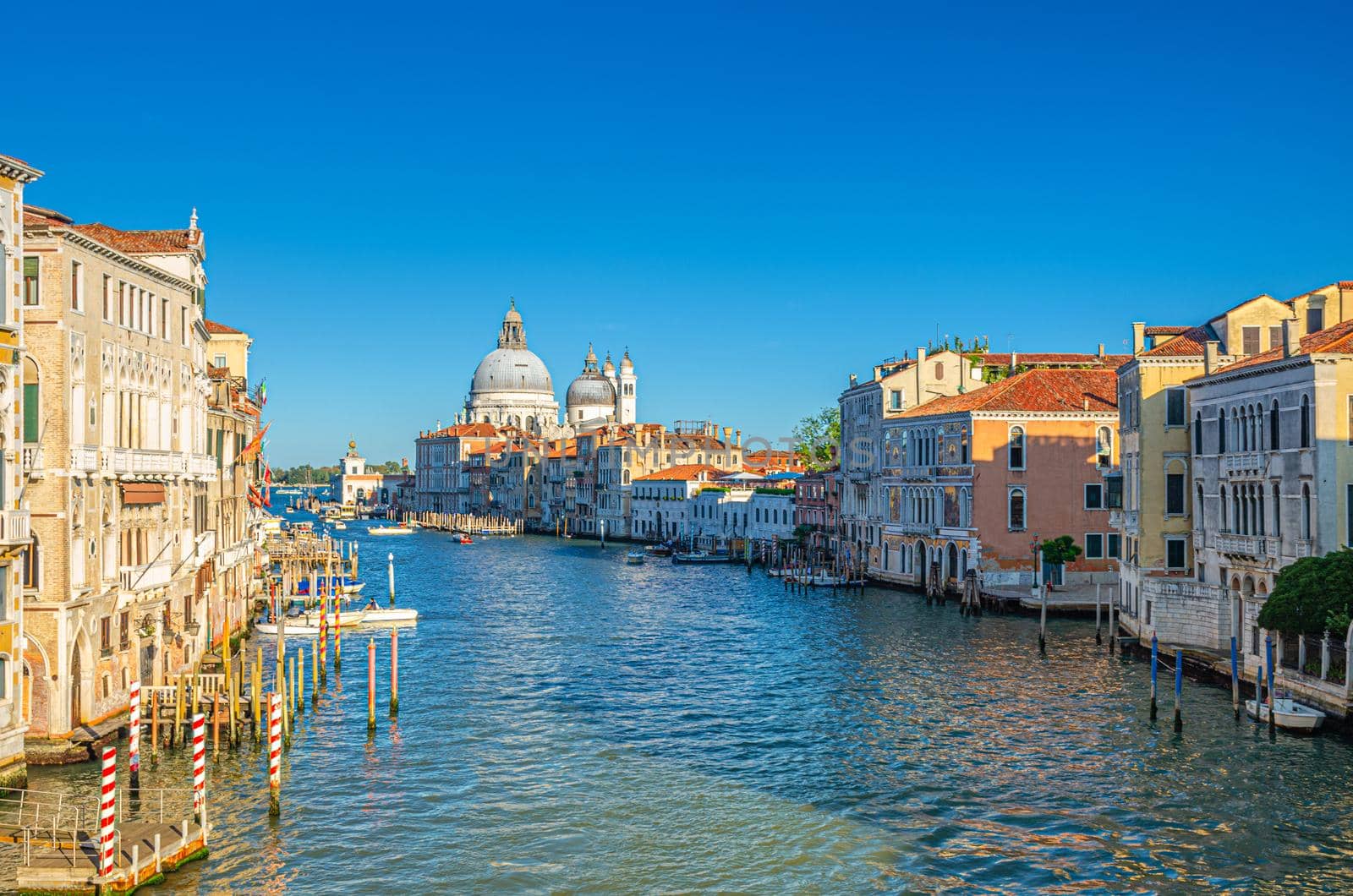 Venice cityscape with Grand Canal waterway Canal Grande in historical city centre. Santa Maria della Salute Roman Catholic church on Punta della Dogana, blue sky background. Veneto Region, Italy.
