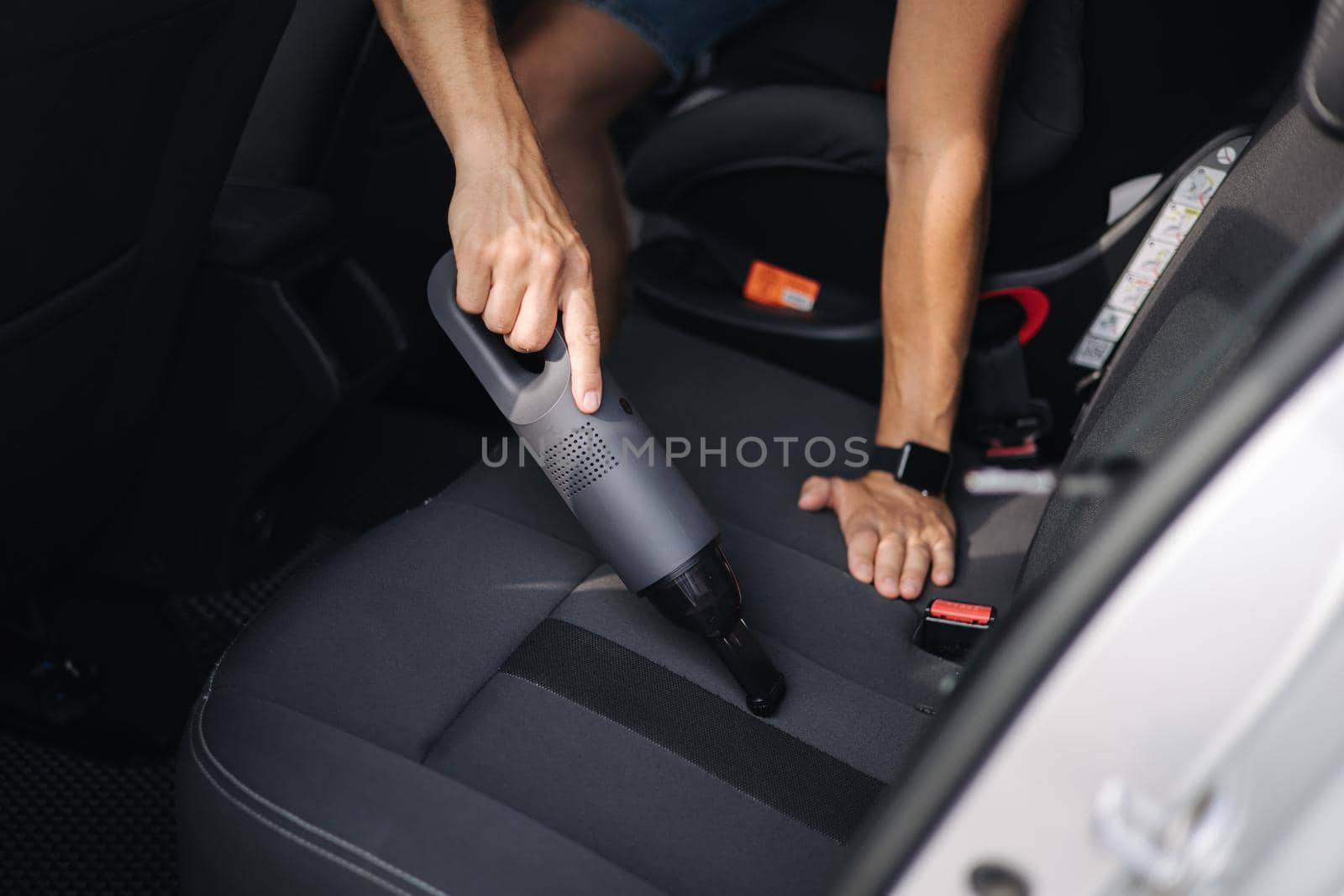 Close up of male using portable vacuum cleaner in her car. Electrical vacuum in man's hand clean car inside from dust.