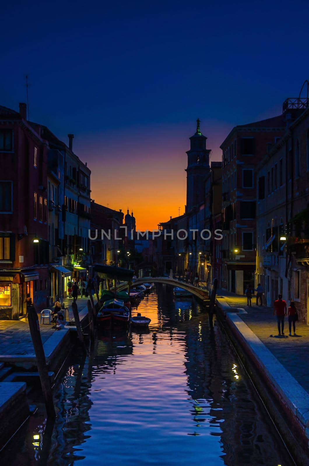 Venice cityscape with narrow water canal, fondamenta embankment. Silhouette of bridge, bell tower and buildings. Veneto Region, Northern Italy. Typical Venetian view at sunset evening, vertical view