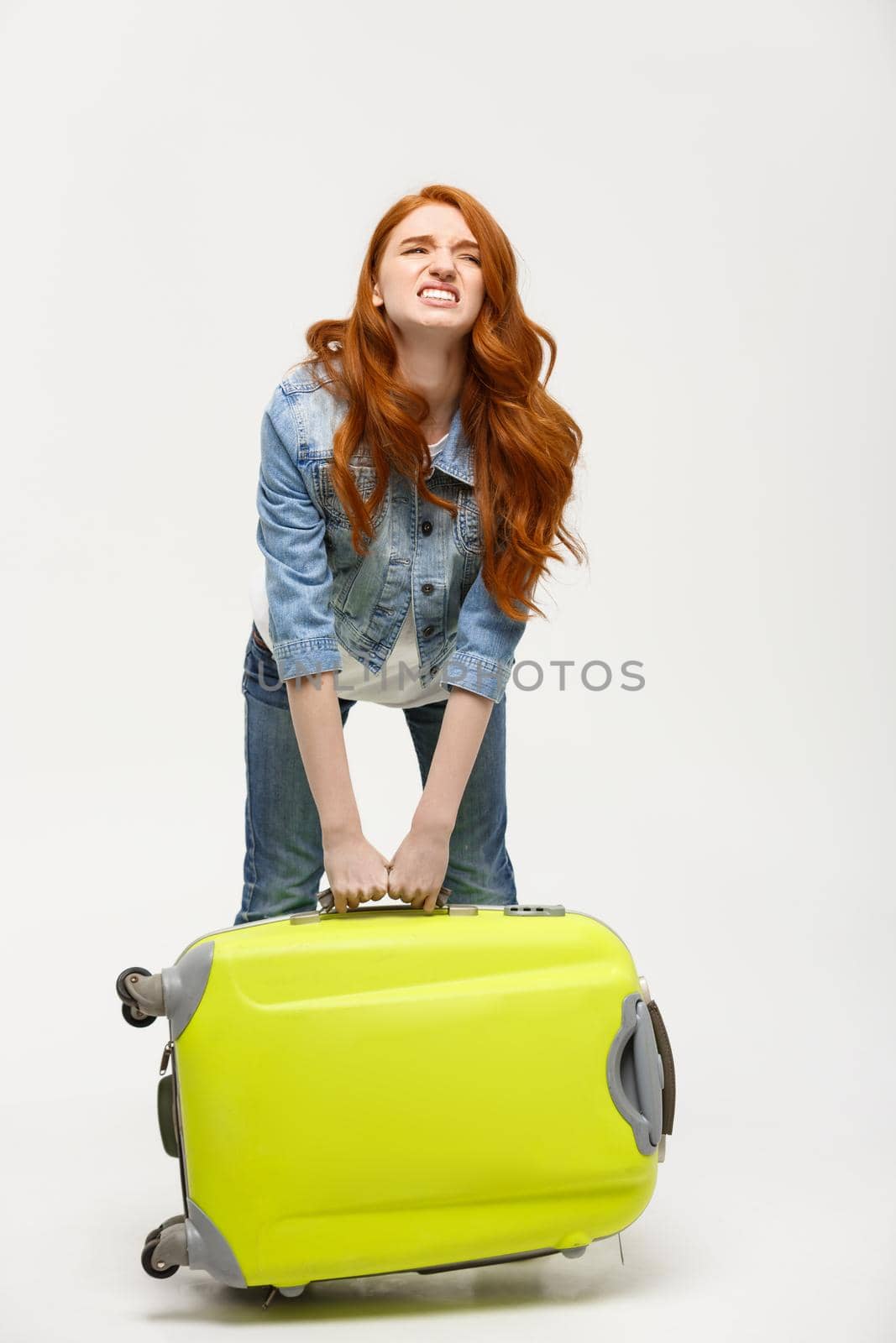 Travel and Lifestyle Concept: Young woman suffers from back pain lifting a heavy suitcase isolated on yellow background.