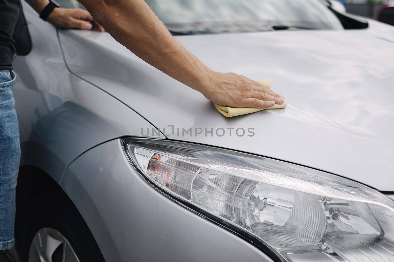 Close-up of handsome man wipes a car with a rag in a showroom at a self-service car wash. Gray car. Back view.