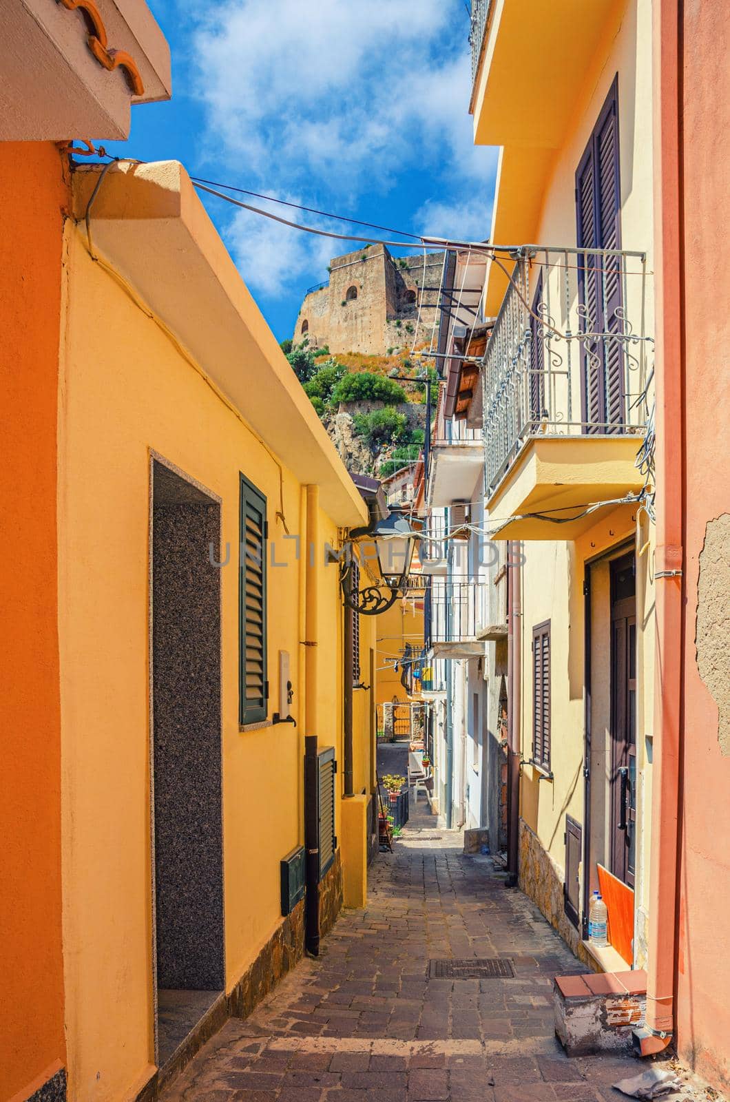 Narrow pedestrian street between buildings with colorful walls in seaside small town Scilla, old medieval castle Castello Ruffo background, Calabria, Southern Italy