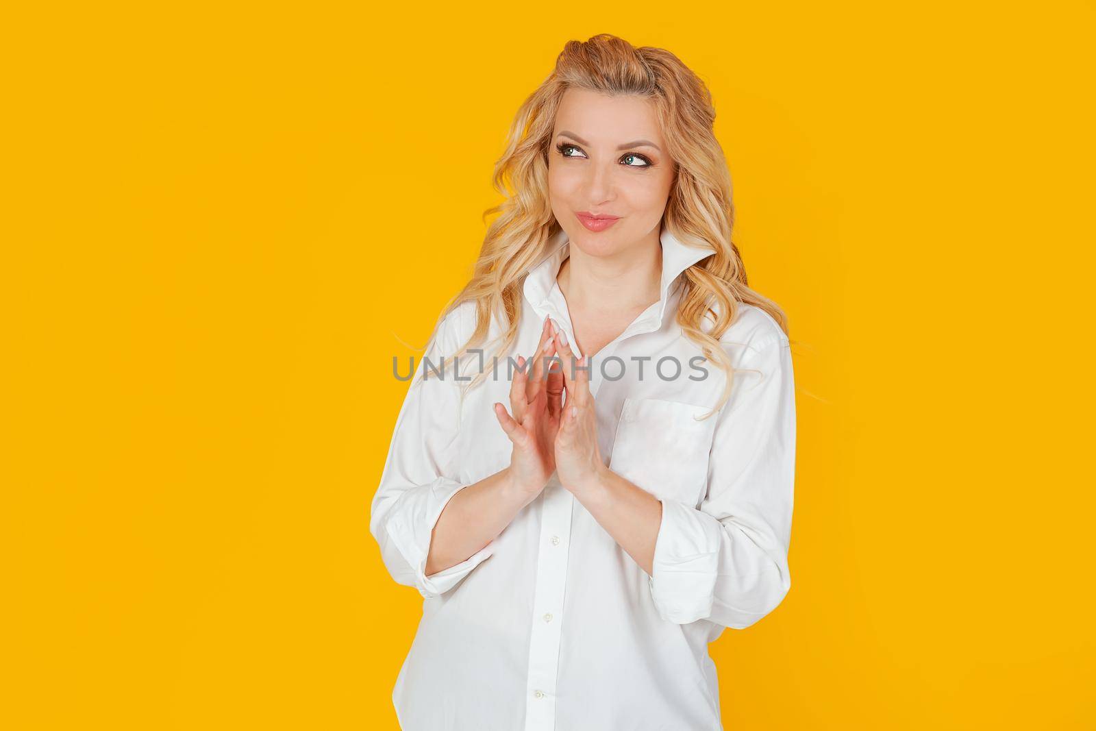 A blonde European woman in a white shirt, as if making a plan in mind, smiling mysteriously, looking to the side, wanting to do something illegal or secretly. I have a great idea. yellow background