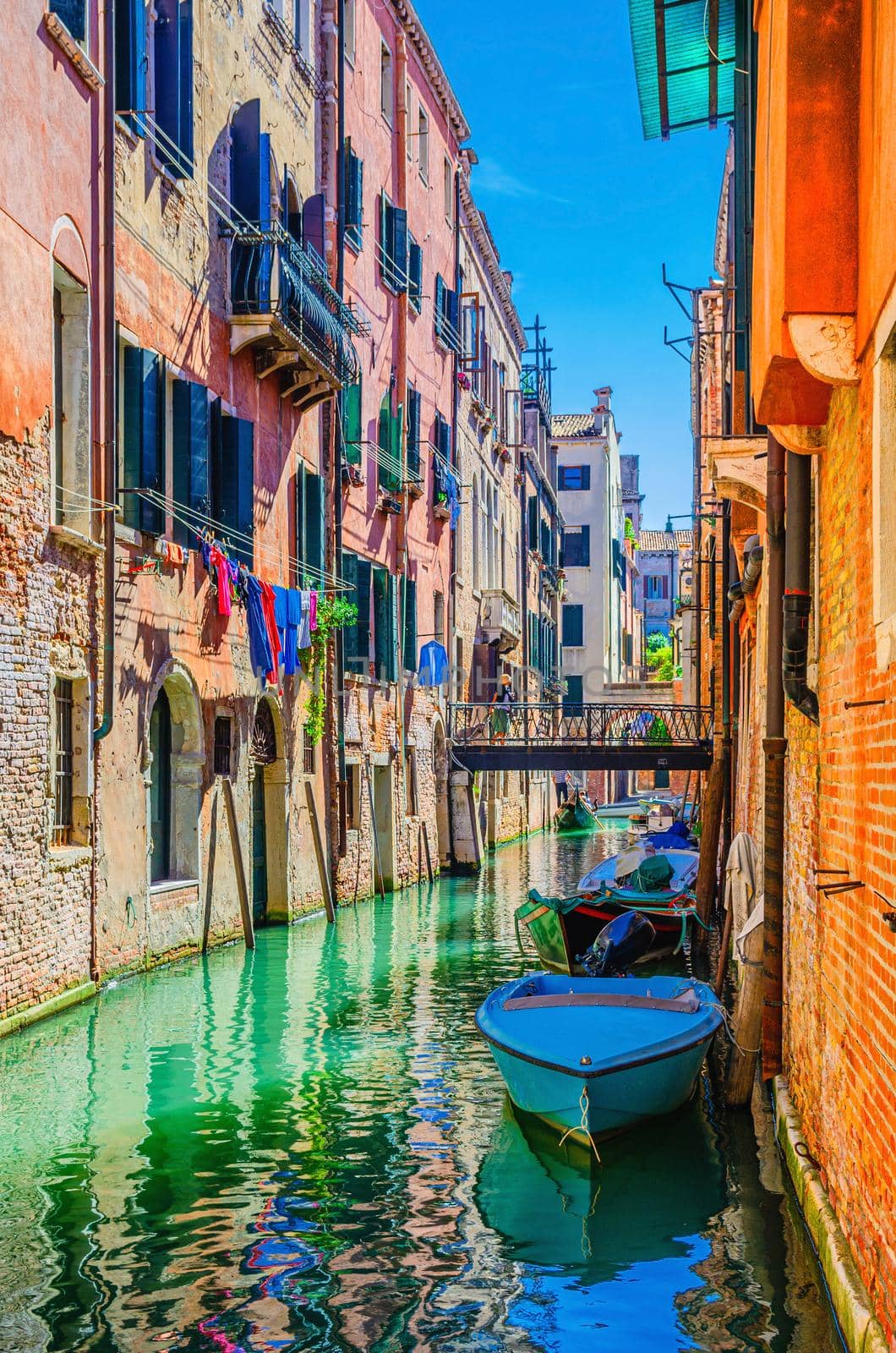 Venice cityscape with narrow water canal with boats moored between old colorful buildings and bridge, Veneto Region, Northern Italy. Typical Venetian view, vertical view, blue sky background