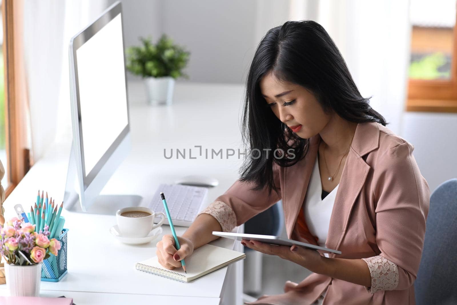 Business woman entrepreneur using digital tablet and making notes on notebook.